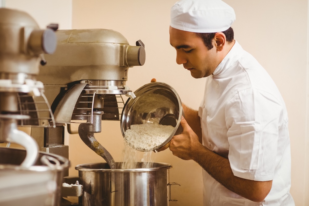 Baker pouring flour into large mixer in a commercial kitchen.jpeg